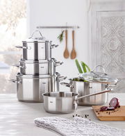 Topfset Paris 5-tlg. aus Edelstahl, bestehend aus vier Töpfen und einer Stielkasserolle mit Glasdeckeln, auf einem Küchentisch arrangiert. Perspektive: seitlich von vorne.