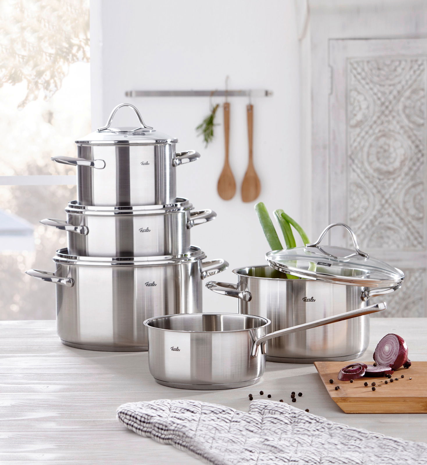 Topfset Paris 5-tlg. aus Edelstahl, bestehend aus vier Töpfen und einer Stielkasserolle mit Glasdeckeln, auf einem Küchentisch arrangiert. Perspektive: seitlich von vorne.