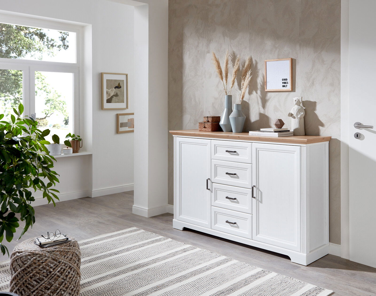 Weißes Sideboard mit Holzplatte, dekoriert mit Vasen und Kunstobjekten, in einem modernen Wohnzimmer mit Blick auf die rechte Seite.