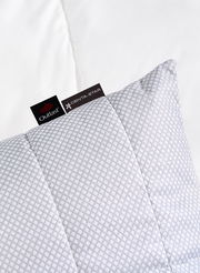 Gestepptes Kissen 80x80cm mit geometrischem Muster, Markenetiketten sichtbar, aus der Vogelperspektive fotografiert.