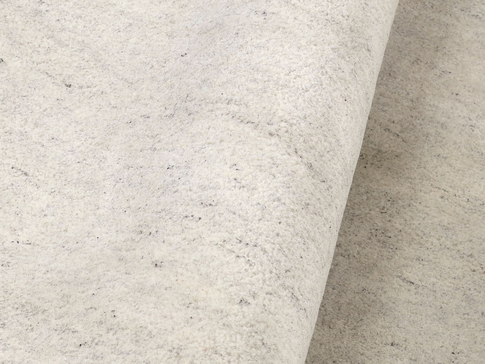 Nahaufnahme eines hellen Wollteppichs mit leicht melierter Textur, von der Seite betrachtet.