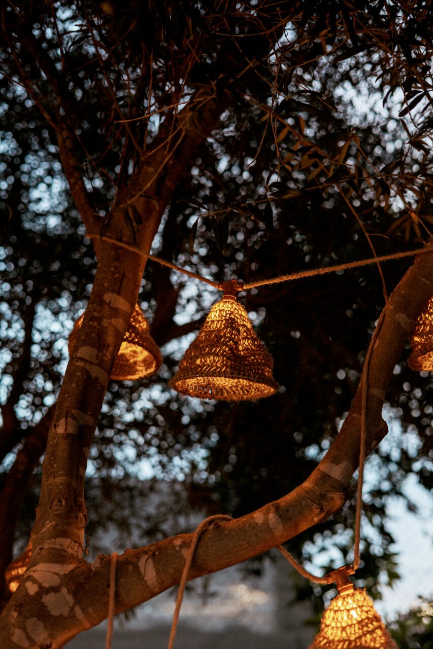 Outdoor-Lichterkette mit geflochtenen Lampenschirmen, aufgehängt an einem Baum in der Abenddämmerung, seitliche Perspektive