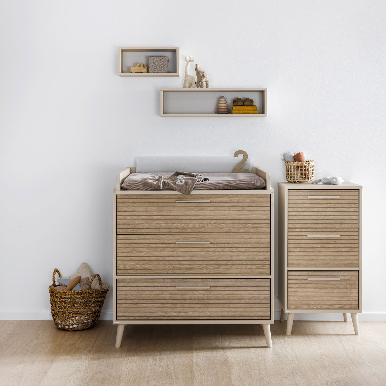 Schmale Kommode aus Holz mit drei Schubladen, neben einer breiteren Kommode mit Wickelauflage, aus der Perspektive von vorne fotografiert.
