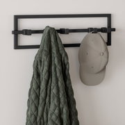 Moderne Wandgarderobe CUBIKO von Umbra in schwarzem Metall mit mehreren Haken, frontal betrachtet, mit einer Jacke und einer Mütze behängt.