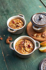 Zwei graue Mini-Cocottes mit gebackenem Dessert, umgeben von Pekannüssen und Apfelscheiben, aus der Vogelperspektive fotografiert.