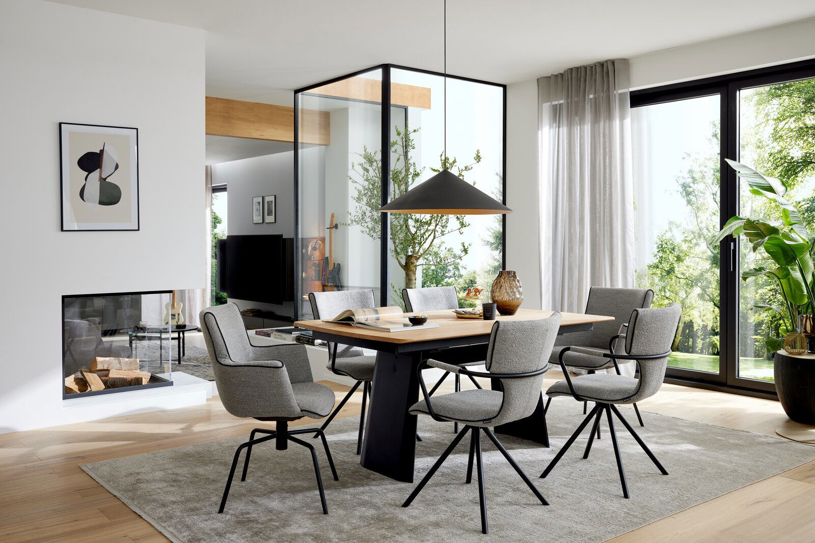 Modernes Esszimmer-Set mit rechteckigem Holztisch und sechs grauen Polsterstühlen mit schwarzen Metallbeinen, darüber eine schwarze Pendelleuchte; Perspektive: frontale, leicht seitliche Weitwinkelansicht auf Tischgruppe im hellen Raum mit großen Fenstern