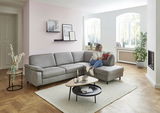 Graue Polsterrundecke in einem modernen Wohnzimmer, seitliche Perspektive, mit einer Person, die auf dem Sofa sitzt und ein Buch liest.
