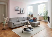 Graue Polsterrundecke in einem modernen Wohnzimmer, seitliche Perspektive, mit einer Person, die auf dem Sofa sitzt und ein Buch liest.