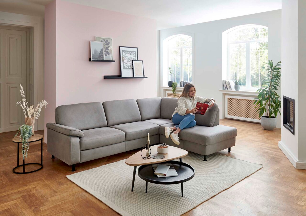 Grijze hoekbank in een moderne woonkamer, gezien vanaf de zijkant, met iemand die op de bank zit en een boek leest.