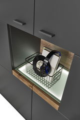 Nahaufnahme eines modernen Highboards mit dunklen Schranktüren und einem offenen Fach mit Beleuchtung, das einen Korb mit Schallplatten und Kopfhörern enthält. Perspektive von schräg oben.