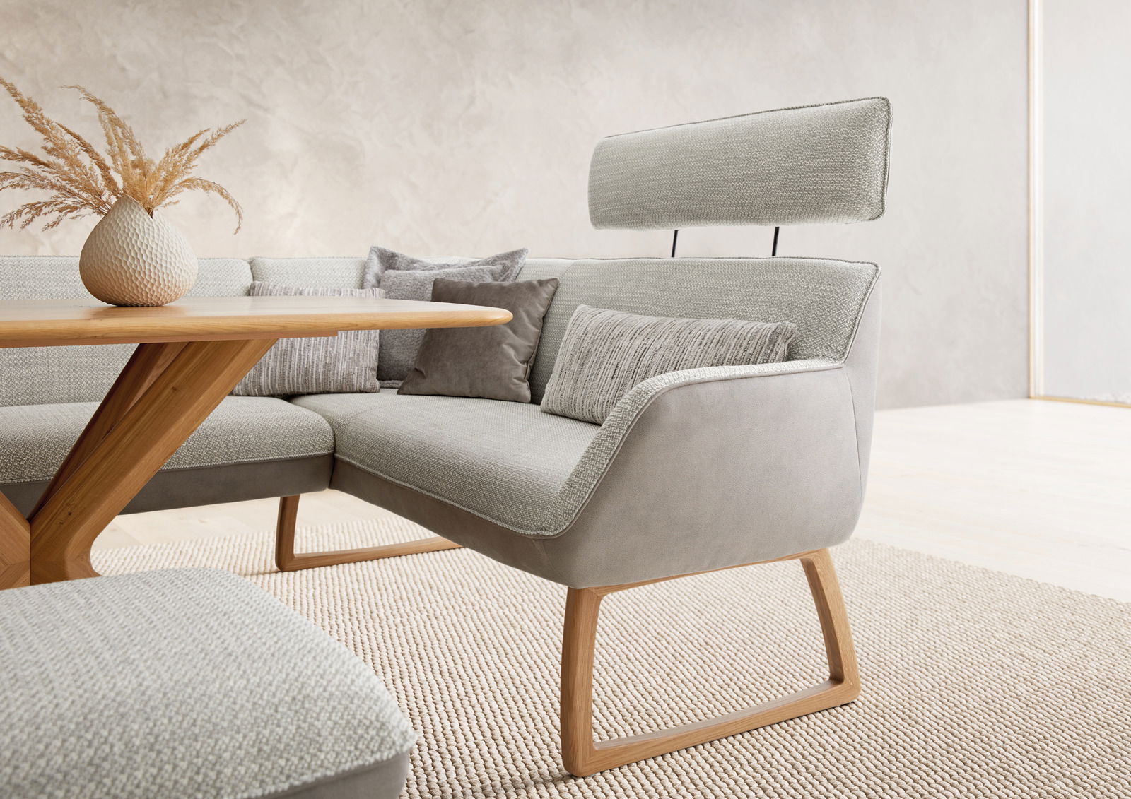 Moderne Eckbank mit grauem Stoffbezug und Holzgestell, seitliche Perspektive. Dekoriert mit Kissen und einer Vase auf einem Holztisch.