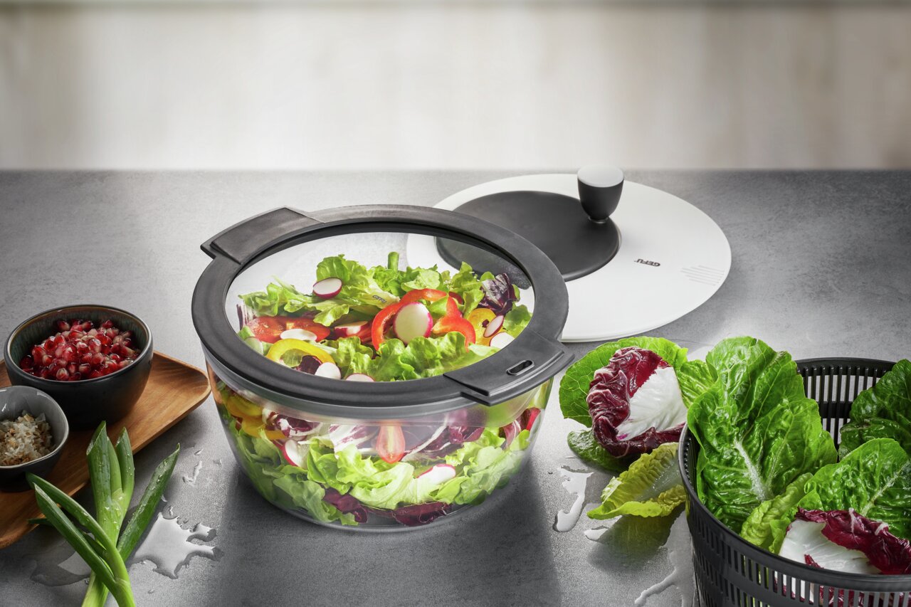 Salatschleuder ROTARE mit frischem Salat, von oben fotografiert, umgeben von Zutaten wie Granatapfelkernen und Frühlingszwiebeln.