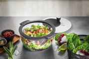 Salatschleuder ROTARE mit frischem Salat, von oben fotografiert, umgeben von Zutaten wie Granatapfelkernen und Frühlingszwiebeln.