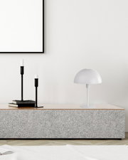 Moderne Tischleuchte MEIKE in Weiß auf einem grauen Sideboard, seitliche Perspektive