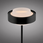 Moderne schwarze Außen-Stehleuchte mit ringförmigem Schirm und opalem Diffusor, warmweiß leuchtend, Nahaufnahme von schräg oben vor grauem Hintergrund