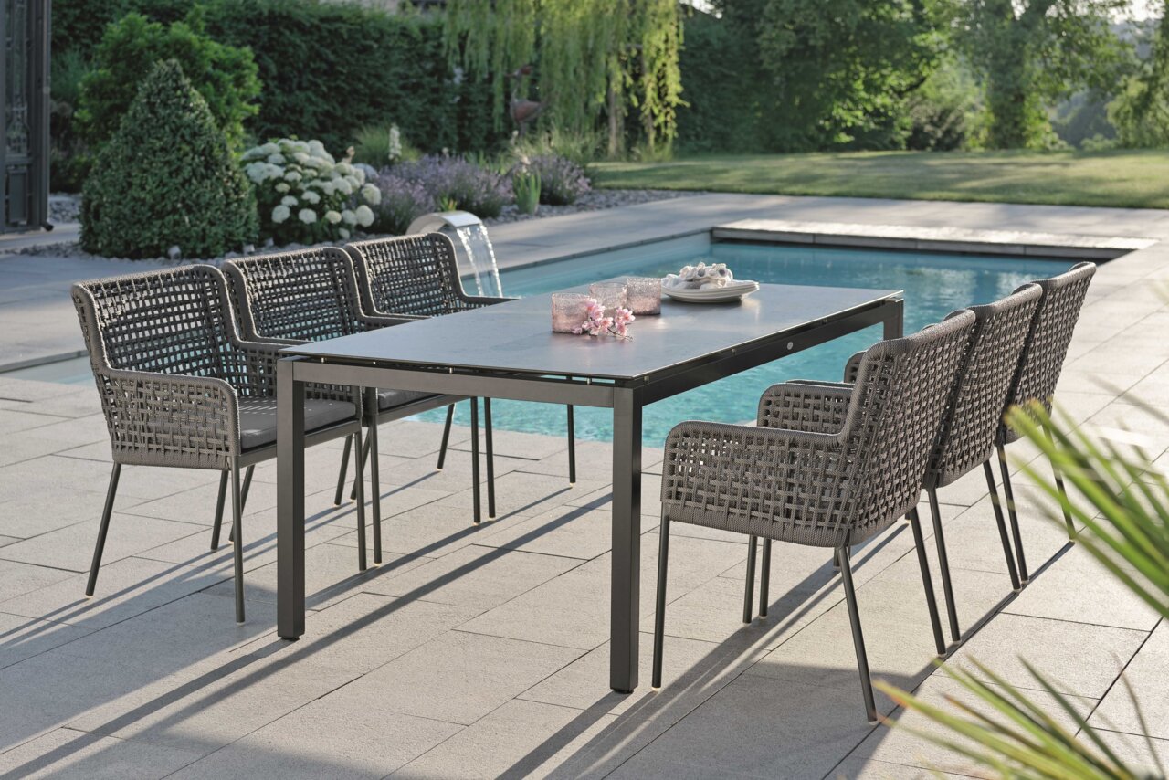Moderner Diningsessel aus geflochtenem Material, Teil eines stilvollen Outdoor-Essbereichs am Pool, seitliche Perspektive.