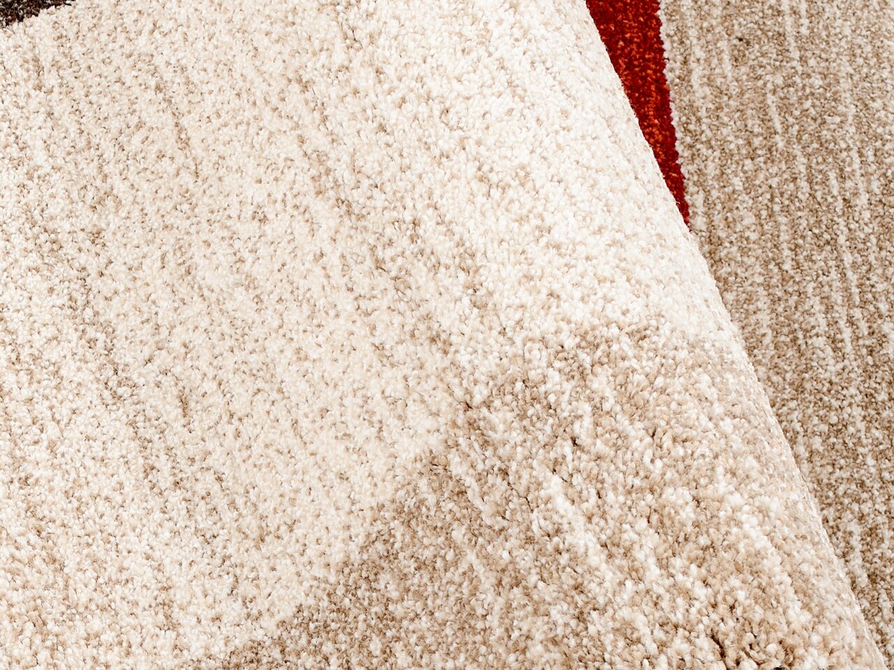 Nahaufnahme eines strukturierten Teppichs in Beige- und Brauntönen mit einem Hauch von Rot, perspektivisch von oben betrachtet.