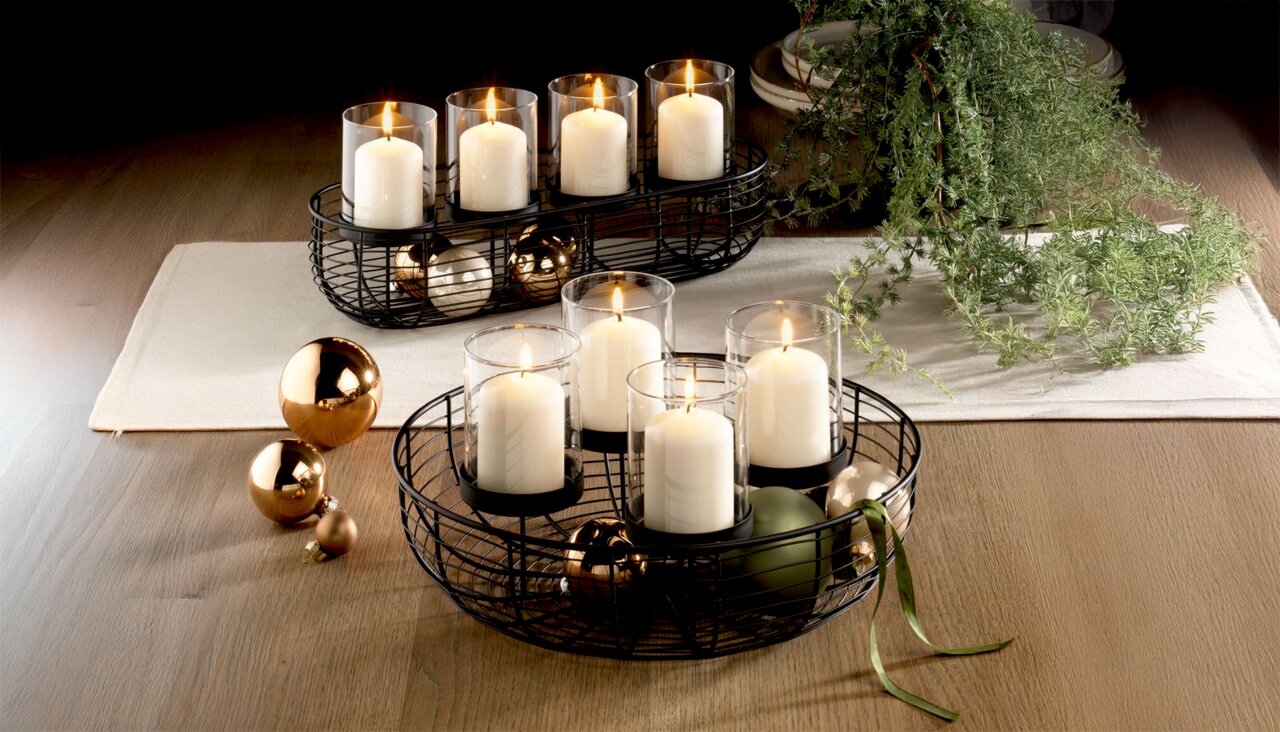 Dekorativer runder Kranz mit vier weißen Kerzen in Glaszylindern, umgeben von goldenen und grünen Kugeln, auf einem Holztisch von oben betrachtet.