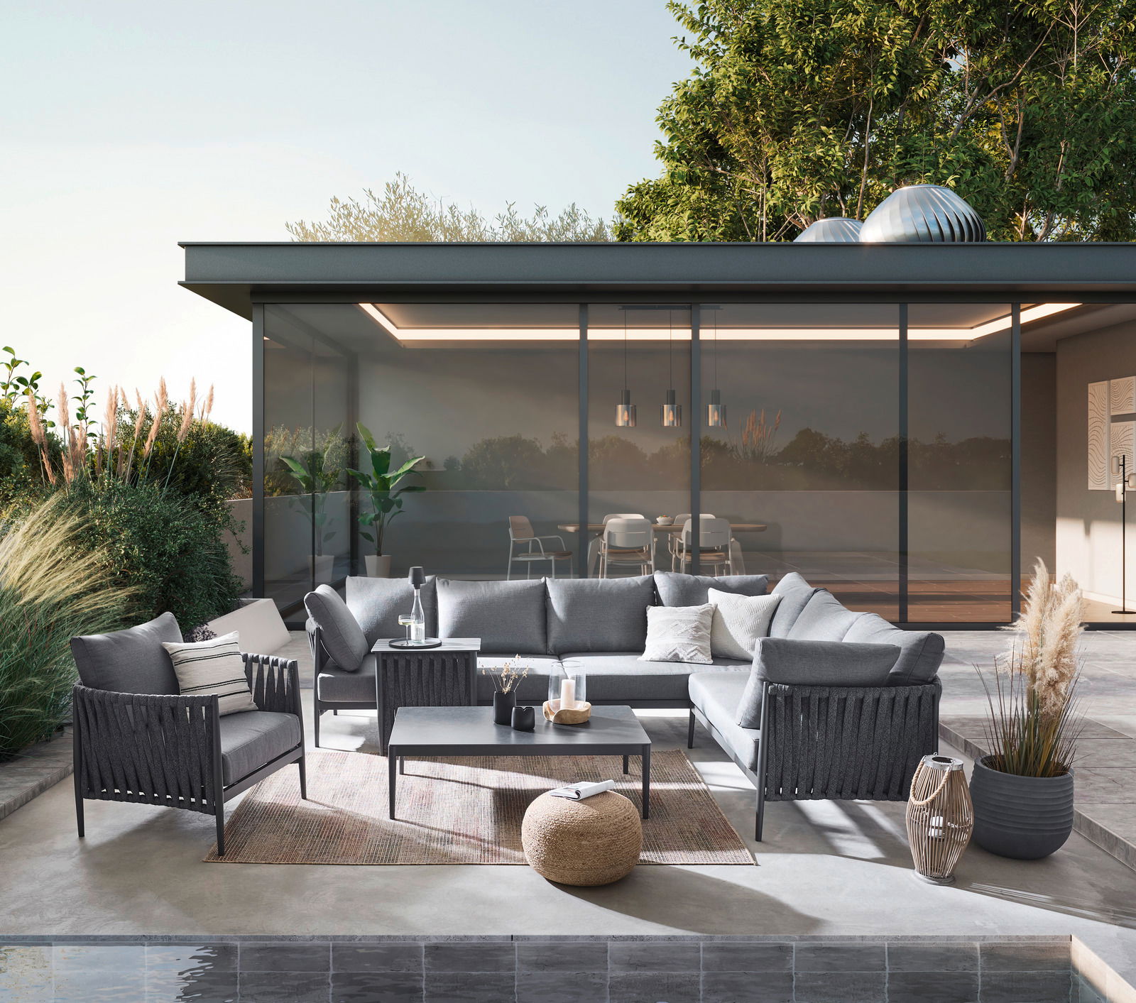 Moderner Loungetisch auf einer stilvollen Terrasse, umgeben von eleganten grauen Sofas und Sesseln, mit Blick auf einen modernen Glasbau im Hintergrund.