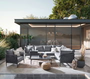 Moderner Loungetisch auf einer stilvollen Terrasse, umgeben von eleganten grauen Sofas und Sesseln, mit Blick auf einen modernen Glasbau im Hintergrund.