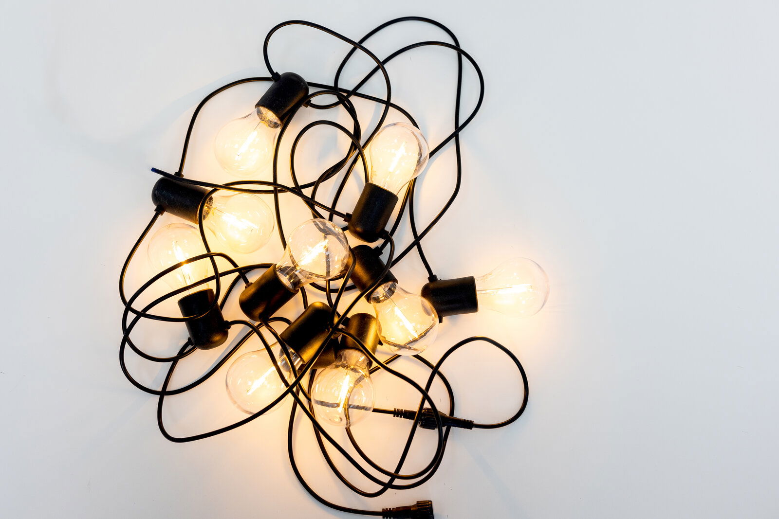 Leuchtende Lichterkette mit mehreren warmweißen Glühbirnen an schwarzem Kabel, von oben (Draufsicht) auf weißem Hintergrund fotografiert