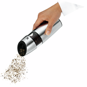 Hand hält eine elektrische Pfeffermühle aus Edelstahl, die Pfefferkörner mahlt. Perspektive von der Seite.