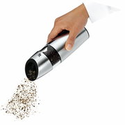 Hand hält eine elektrische Pfeffermühle aus Edelstahl, die Pfefferkörner mahlt. Perspektive von der Seite.