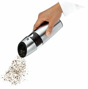 Hand hält eine elektrische Pfeffermühle aus Edelstahl, die Pfefferkörner mahlt. Perspektive von der Seite.