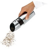 Hand hält eine elektrische Pfeffermühle aus Edelstahl, die Pfefferkörner mahlt. Perspektive von der Seite.