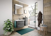 Modernes Badezimmer mit grauem Badblock, bestehend aus einem Waschbeckenunterschrank und einem hohen Schrank, beide in Holzoptik. Perspektive von vorne, mit Blick auf den Waschtisch und den Spiegel.