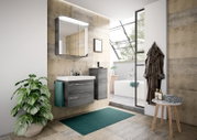 Modernes Badezimmer mit grauem Badblock, bestehend aus einem Waschbeckenunterschrank und einem hohen Schrank, beide in Holzoptik. Perspektive von vorne, mit Blick auf den Waschtisch und den Spiegel.