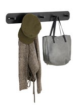 Schwarze Hakenleiste mit mehreren Haken, an denen eine grüne Mütze, ein grauer Pullover und eine graue Tasche hängen. Frontalansicht.