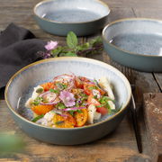 Nahaufnahme eines Geschirrsets Terra in Azur mit einem dekorativen Salat in einer Schale, umgeben von weiteren Schalen auf einem rustikalen Holztisch.