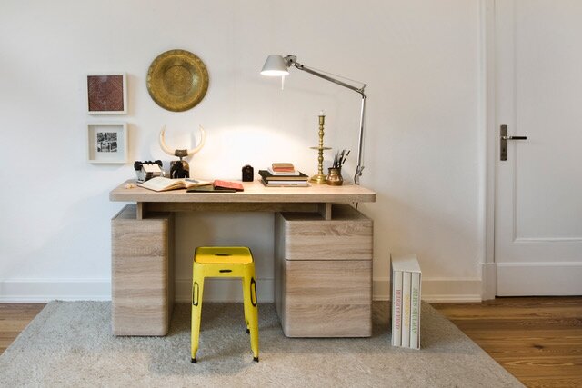 Moderner Schreibtisch aus Holz mit zwei Schubladeneinheiten, gelbem Hocker und Schreibtischlampe, frontal betrachtet.