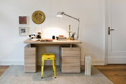 Moderner Schreibtisch aus Holz mit zwei Schubladeneinheiten, gelbem Hocker und Schreibtischlampe, frontal betrachtet.