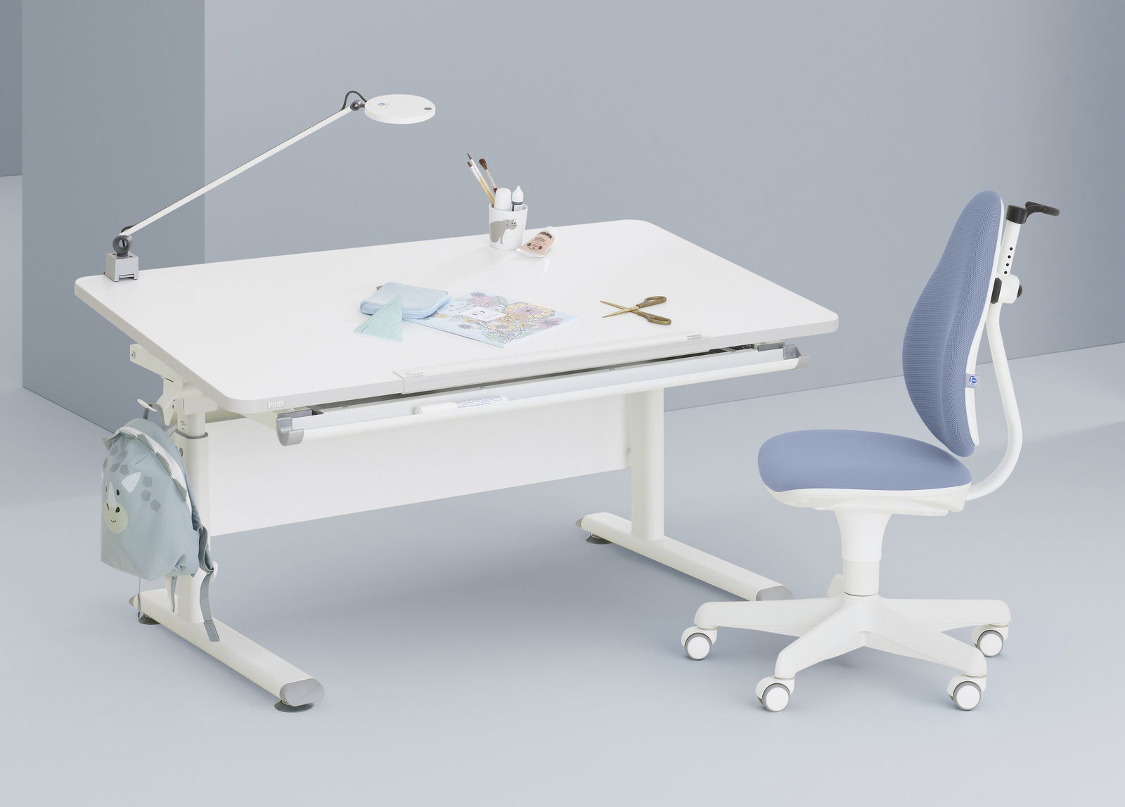 Moderner Jugenddrehstuhl in Blau und Weiß, seitliche Perspektive, neben einem weißen Schreibtisch mit Lampe und Schreibutensilien.