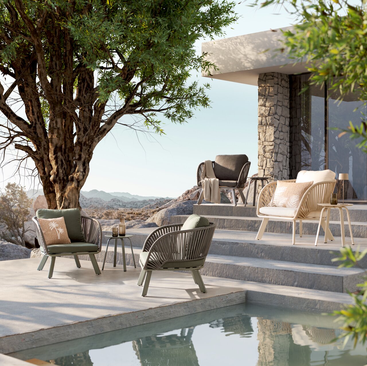 Ambia Garden Loungestoel KATO Moderne Outdoor-Lounge-Möbel auf einer Poolterrasse neben einem Haus mit Natursteinwand, mit Sesseln und Beistelltisch unter einem Baum; Perspektive: seitliche, leicht erhöhte Weitwinkelansicht.