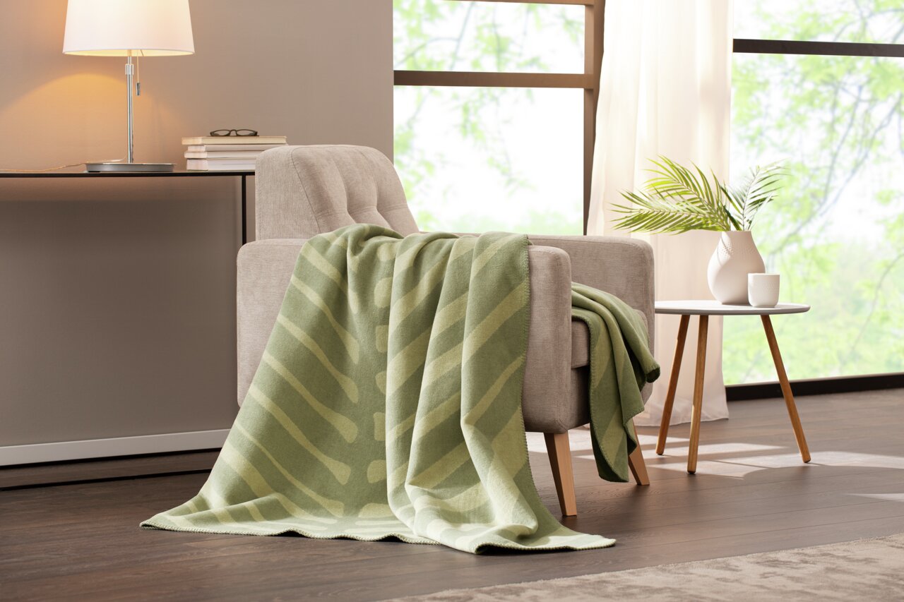 Grüne Wohndecke mit Streifenmuster auf einem beigen Sessel in einem modernen Wohnzimmer, seitliche Perspektive