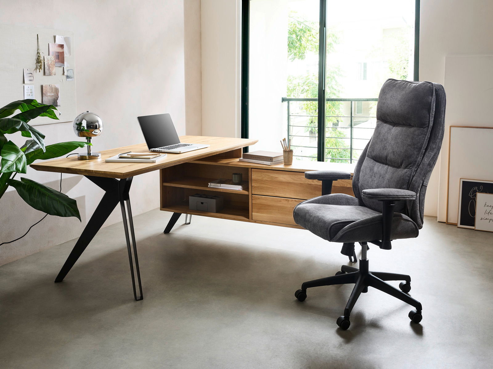 Moderner Eck-Schreibtisch aus Holz mit schwarzem Metallgestell, seitlich von einem bequemen grauen Bürostuhl begleitet, in einem hellen Raum mit großen Fenstern.