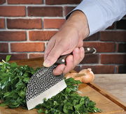 Kochmesser KEEPER 12 cm in der Hand, schneidet frische Kräuter auf einem Holzbrett, seitliche Perspektive.