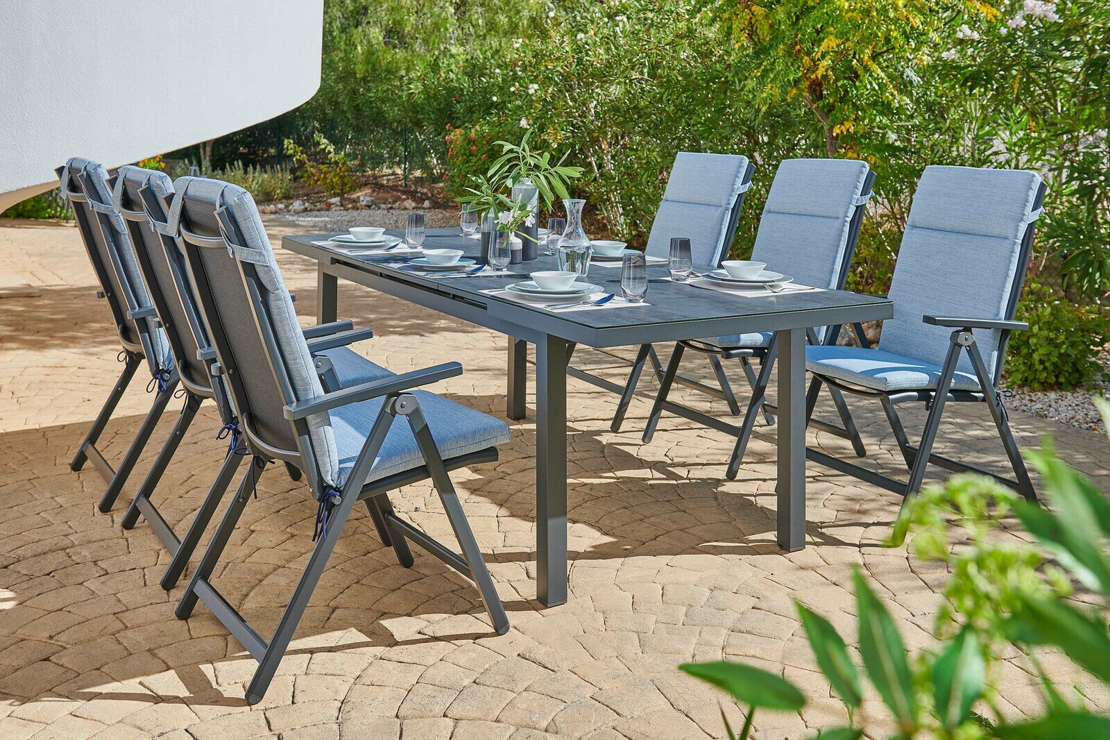 Sechs blaue Klappsessel um einen gedeckten Gartentisch auf einer Terrasse, seitliche Perspektive