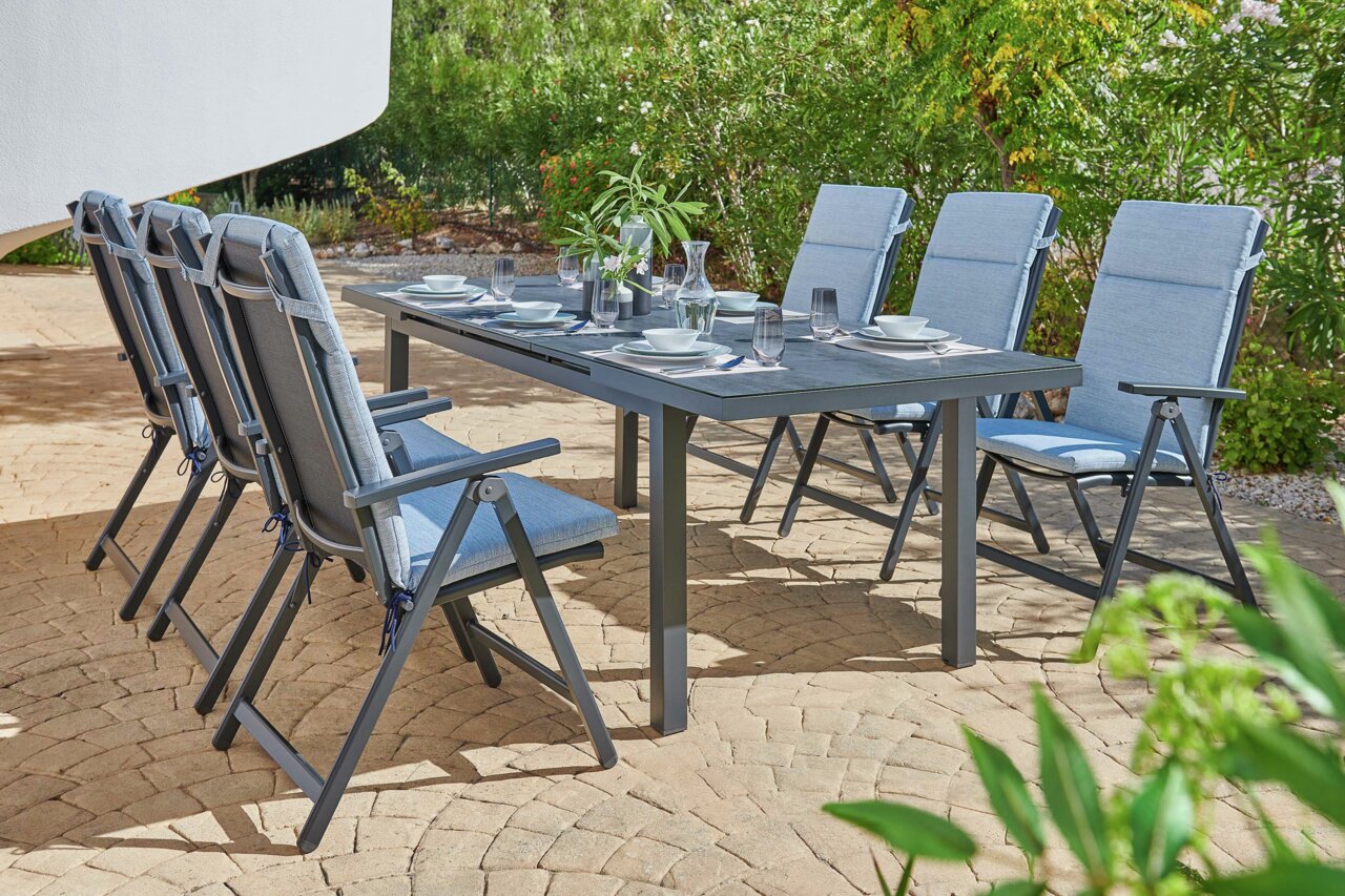 Sechs blaue Klappsessel um einen gedeckten Gartentisch auf einer Terrasse, seitliche Perspektive