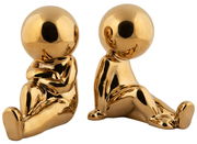 Zwei goldene Buchstützen in Form von stilisierten Figuren, die auf dem Boden sitzen. Die Figuren sind aus glänzendem Material und in einer frontalen Perspektive abgebildet.