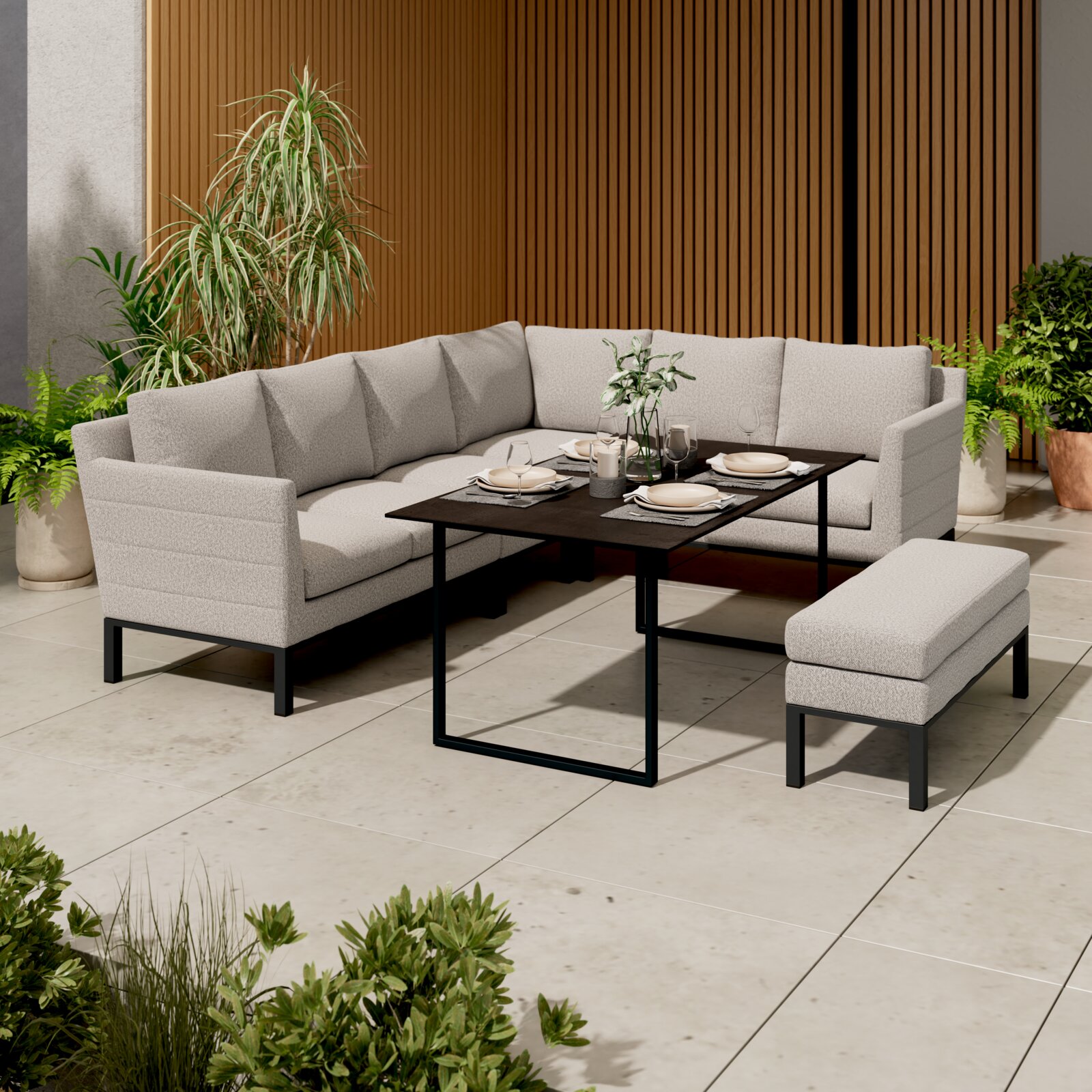Helle, gepolsterte Outdoor-Lounge-Eckgruppe mit schwarzen Metallfüßen und passendem Hocker um einen schwarzen rechteckigen Gartentisch auf einer modernen Terrasse, Perspektive: leicht erhöhte Frontansicht von schräg vorn.