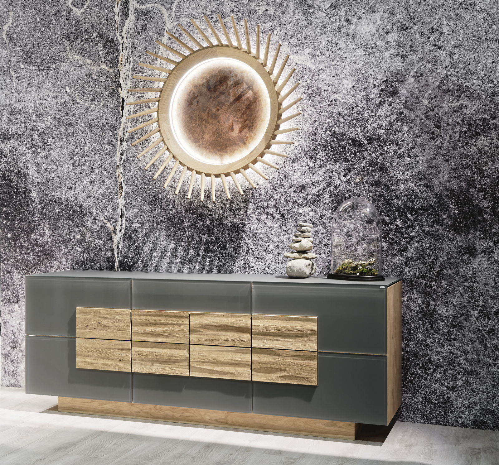 Voglauer Sideboard VMONTANARA Modernes Sideboard in Grau mit Holzelementen, dekoriert mit Steinen und Pflanzen, vor einer strukturierten Wand, aus frontaler Perspektive.