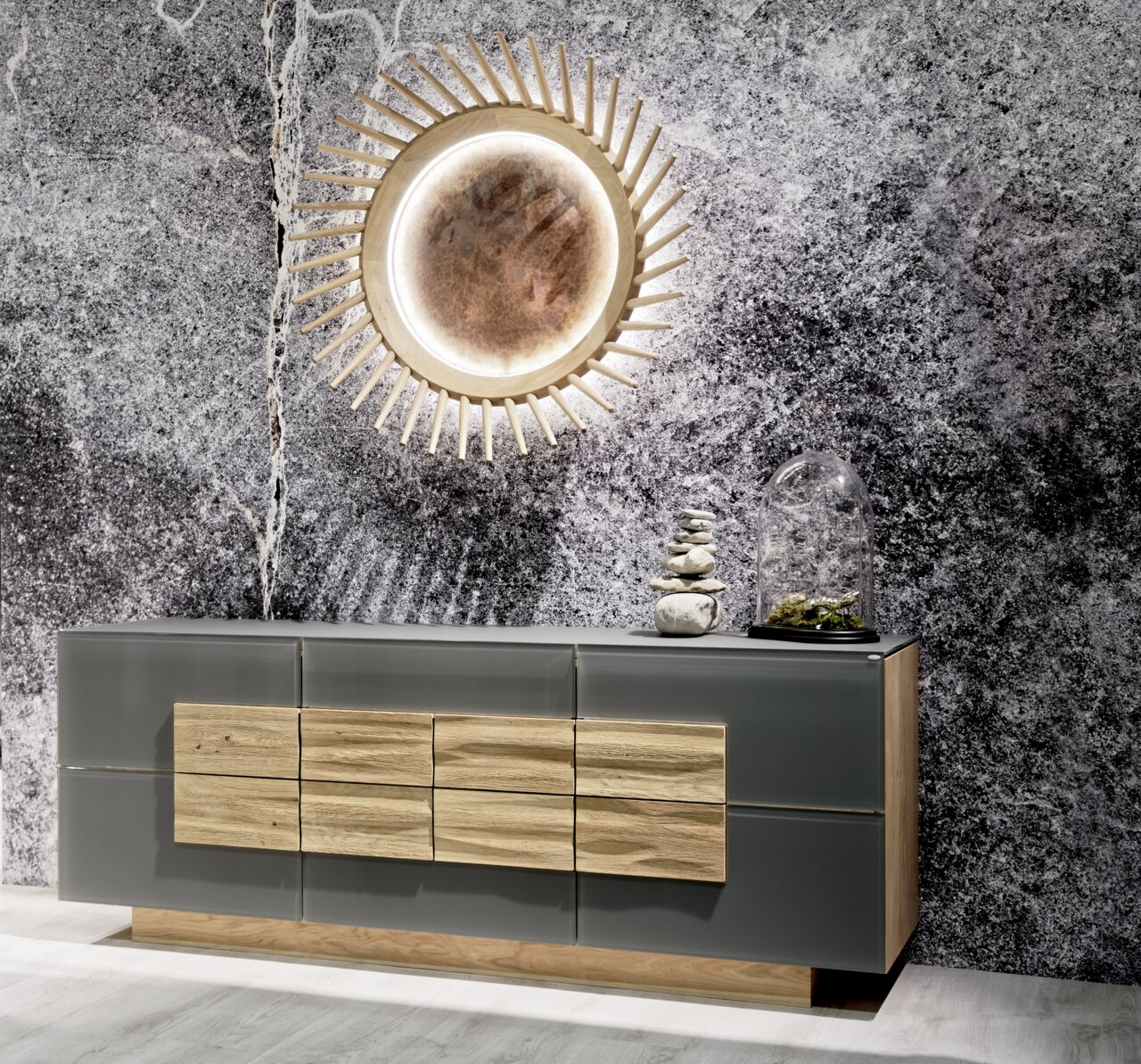 Modernes Sideboard in Grau mit Holzelementen, dekoriert mit Steinen und Pflanzen, vor einer strukturierten Wand, aus frontaler Perspektive.
