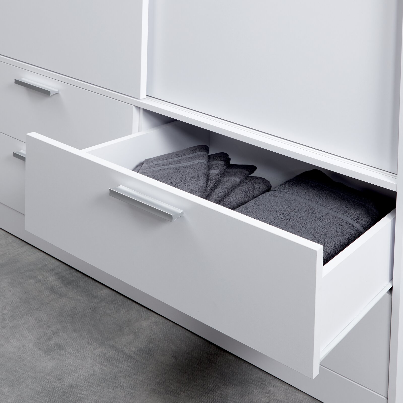 Nahaufnahme eines weißen Schiebetürenschranks mit geöffnetem Schubfach, gefüllt mit gefalteten grauen Handtüchern.