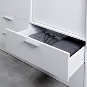 Nahaufnahme eines weißen Schiebetürenschranks mit geöffnetem Schubfach, gefüllt mit gefalteten grauen Handtüchern.