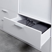 Close-up van een witte kast met schuifdeuren en een geopende lade, gevuld met opgevouwen grijze handdoeken.