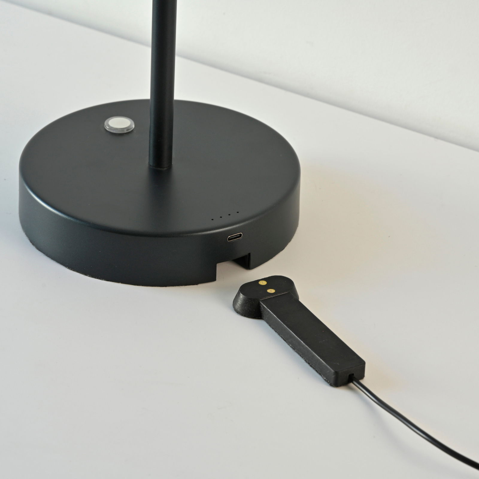 Schwarze Akku-Tischleuchte mit rundem Sockel und USB-Anschluss, seitliche Perspektive.